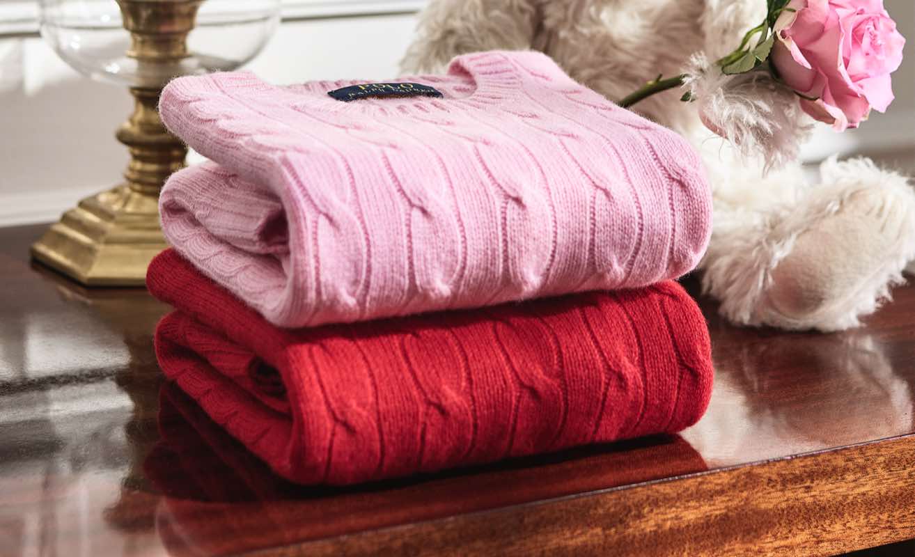 Folded stacked pink and red cable-knit sweaters.