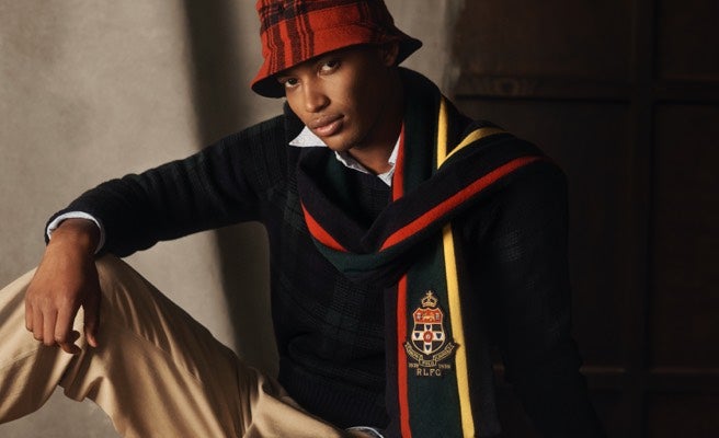 Man in plaid bucket hat & striped scarf with crest patch.