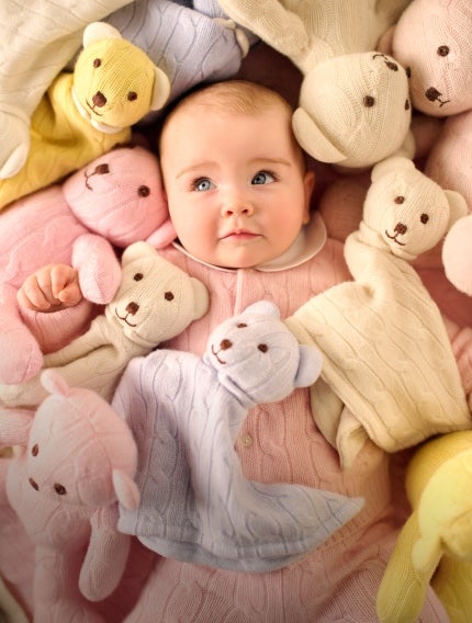 Baby in pink coverall surrounded by toy bears.