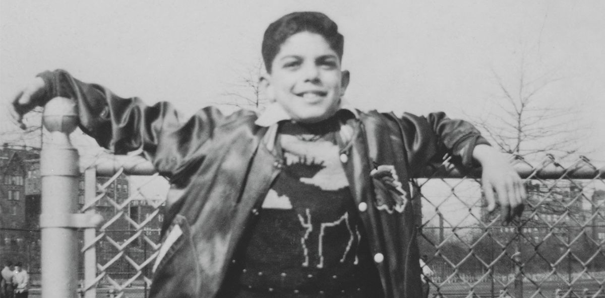 Photograph of a young Ralph Lauren leaning against chain-link fence.