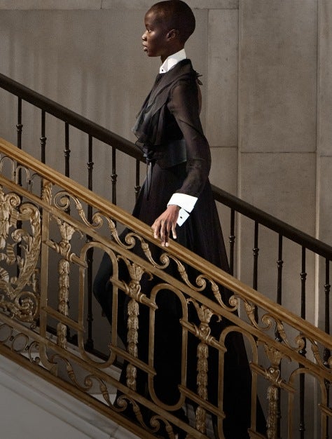 Photograph of model in black Fall 2025 gown on gold staircase.