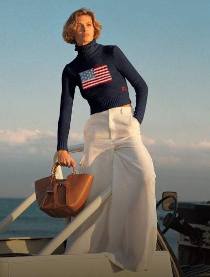 Woman wears navy turtleneck with American flag at front and white wide-leg trousers.