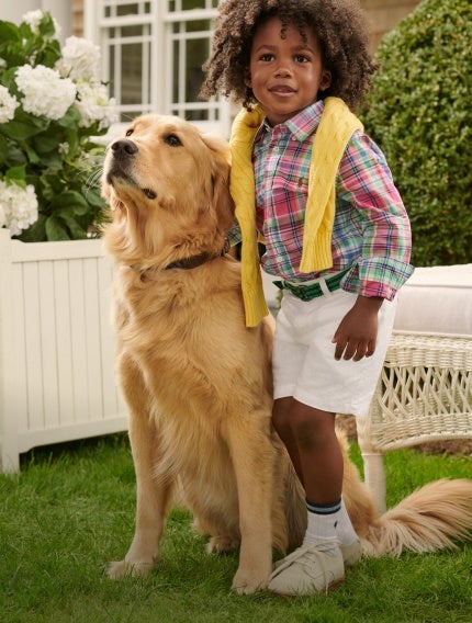 Boy with dog wears a green-and-red plaid shirt and white shorts.