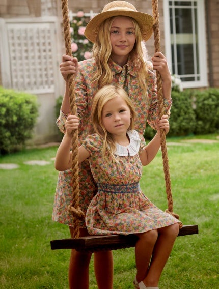 Girls wear matching floral dresses on a swing.