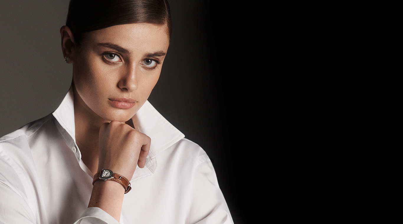 Model wears watch with stirrup-inspired silhouette & brown leather strap