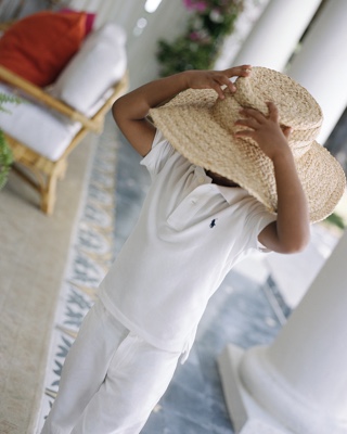 Boy in white Polo shirt trying on adult-size straw hat.