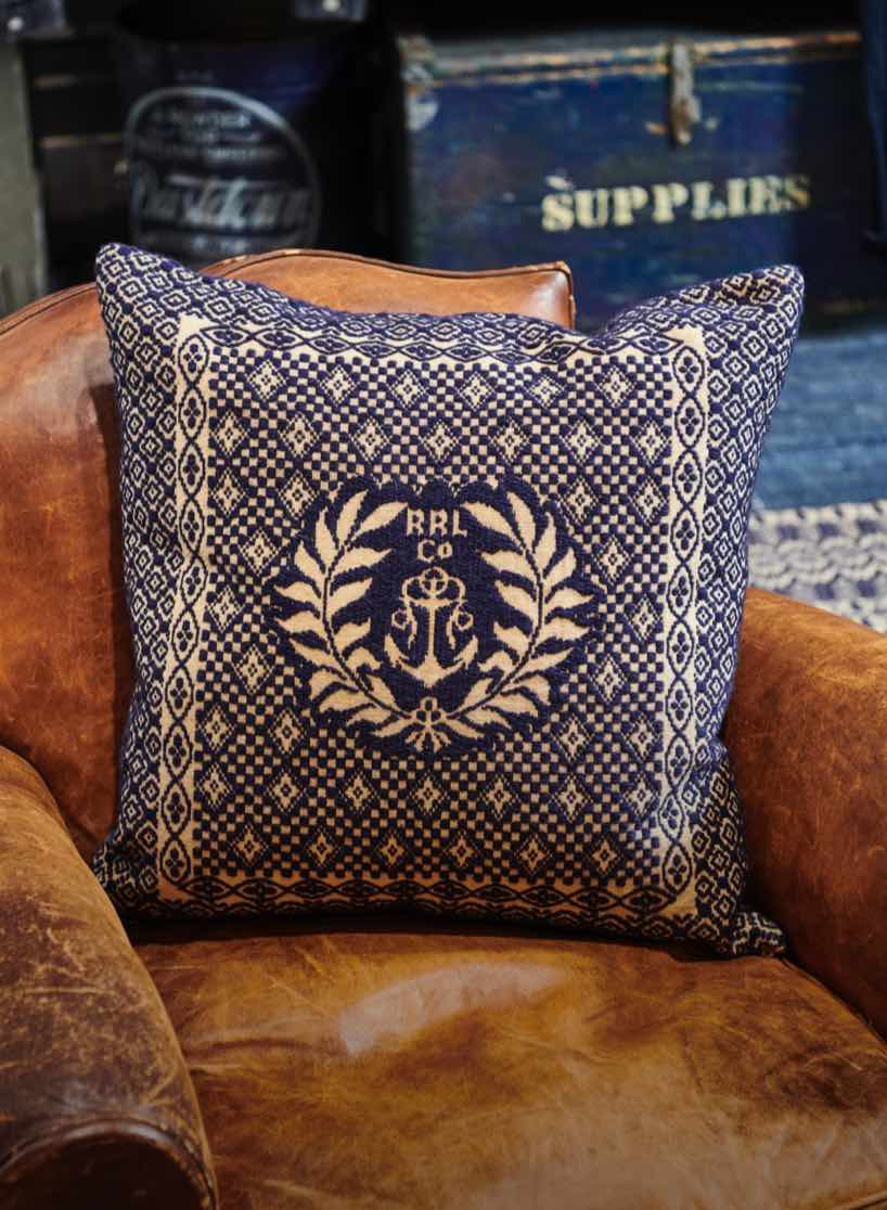 Blue paisley pillow with anchor design on a brown chair.