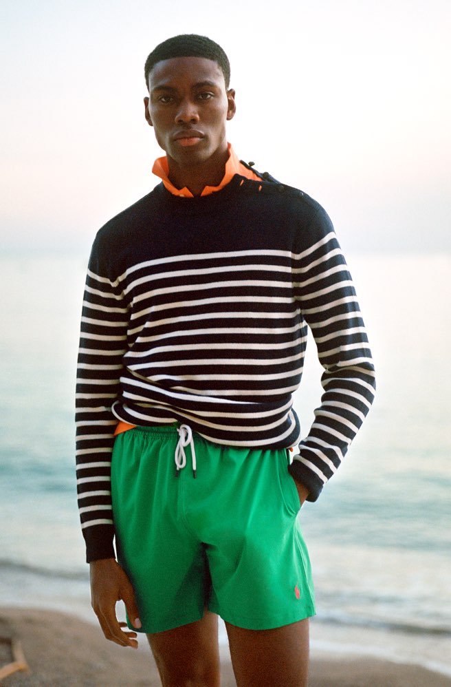 Man wears green drawstring swim trunks & striped sweater