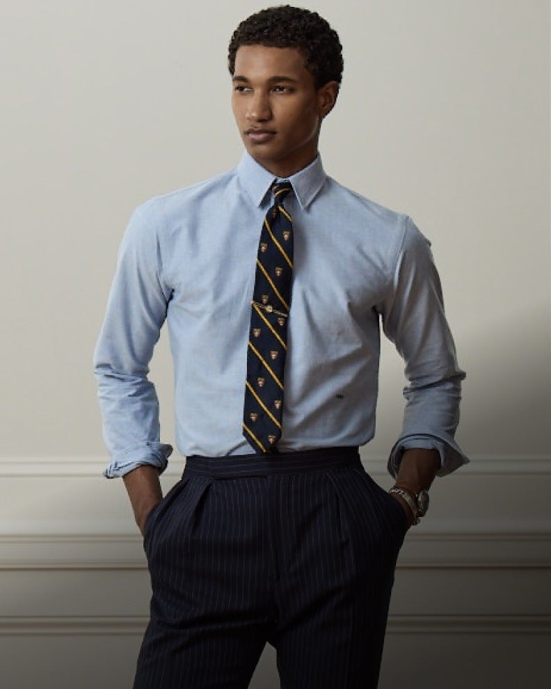 Man wears blue button-down shirt, tie, and navy pinstripe trousers.