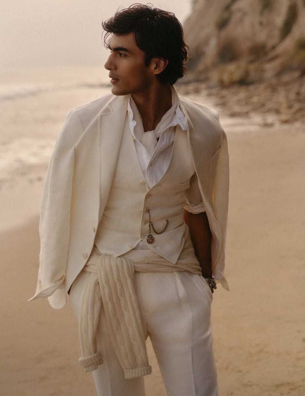 Man on beach wears cream three-piece suit.
