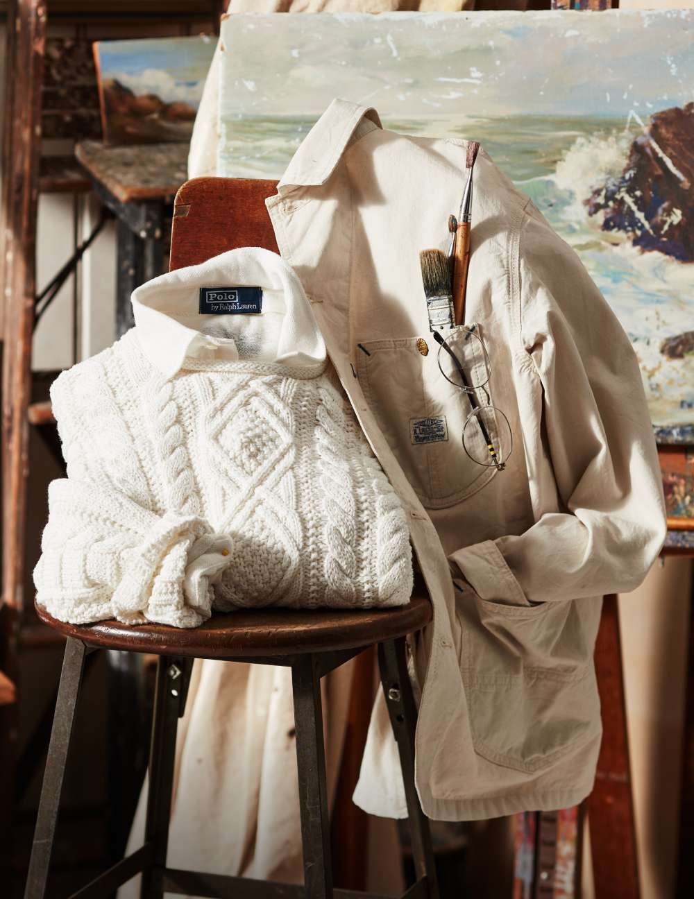 Folded white Aran-knit sweater on chair with white utility jacket.