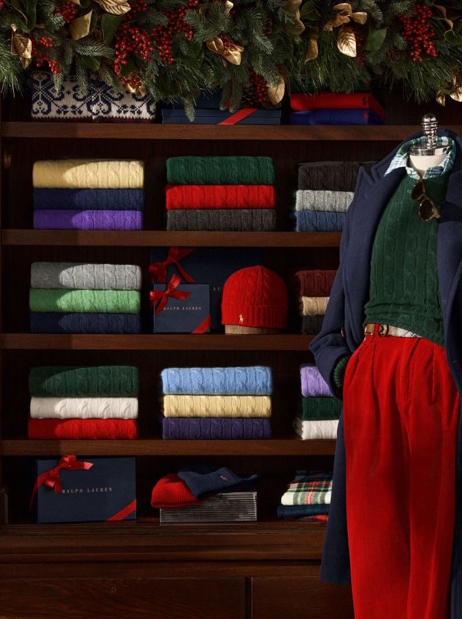 Green cable knit on rig in front of shelves of folded cable-knit sweaters.