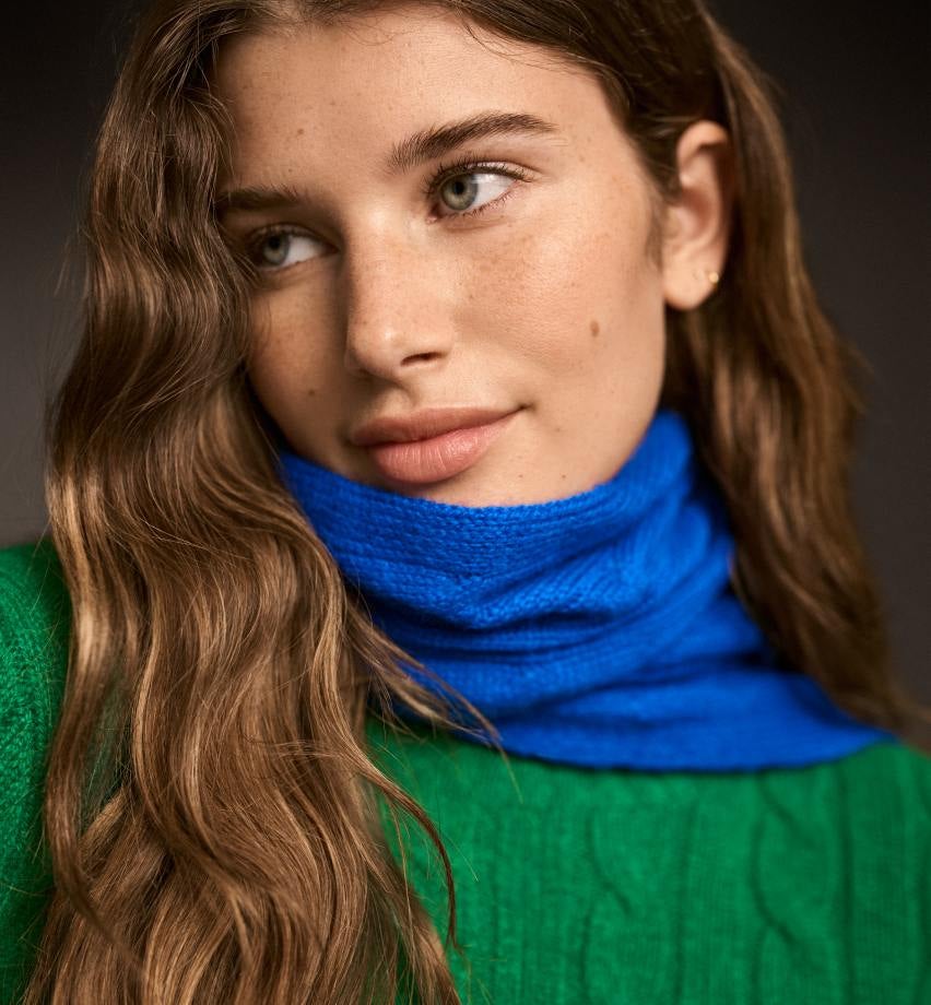 Woman wears blue cable-knit scarf and green cable-knit sweater.