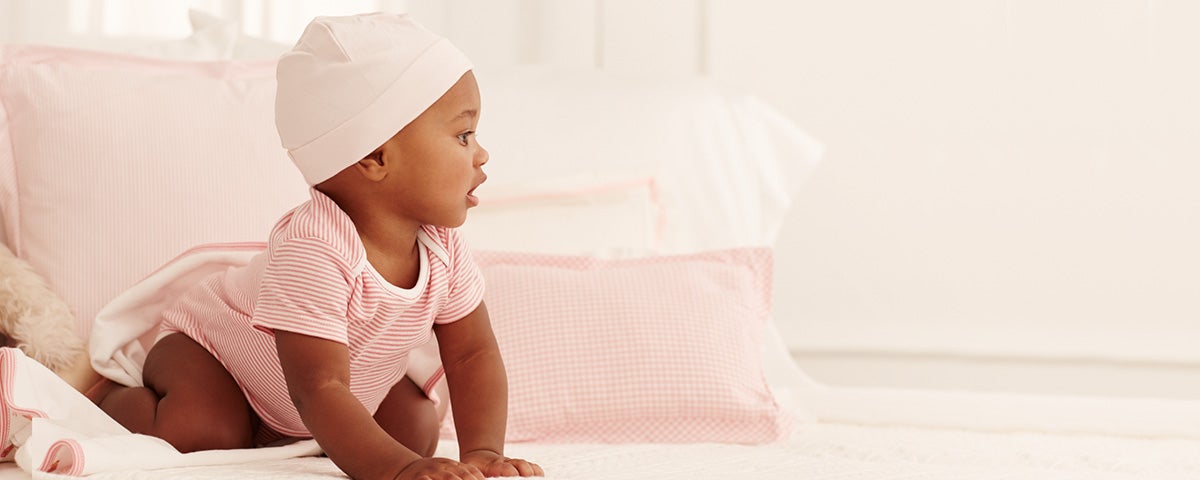 Baby wears pink-and-white striped one-piece and light pink hat.