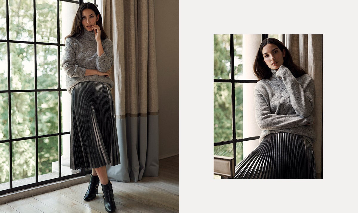 Woman wears grey turtleneck sweater and pleated metallic skirt.