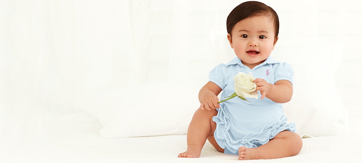 Baby wears light blue ruffled one-piece and holds white rose