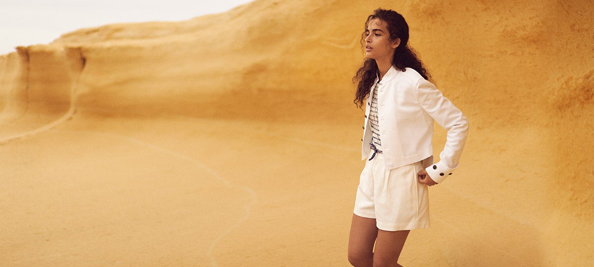 Woman wears white shorts, white jacket, and striped tee in desert.