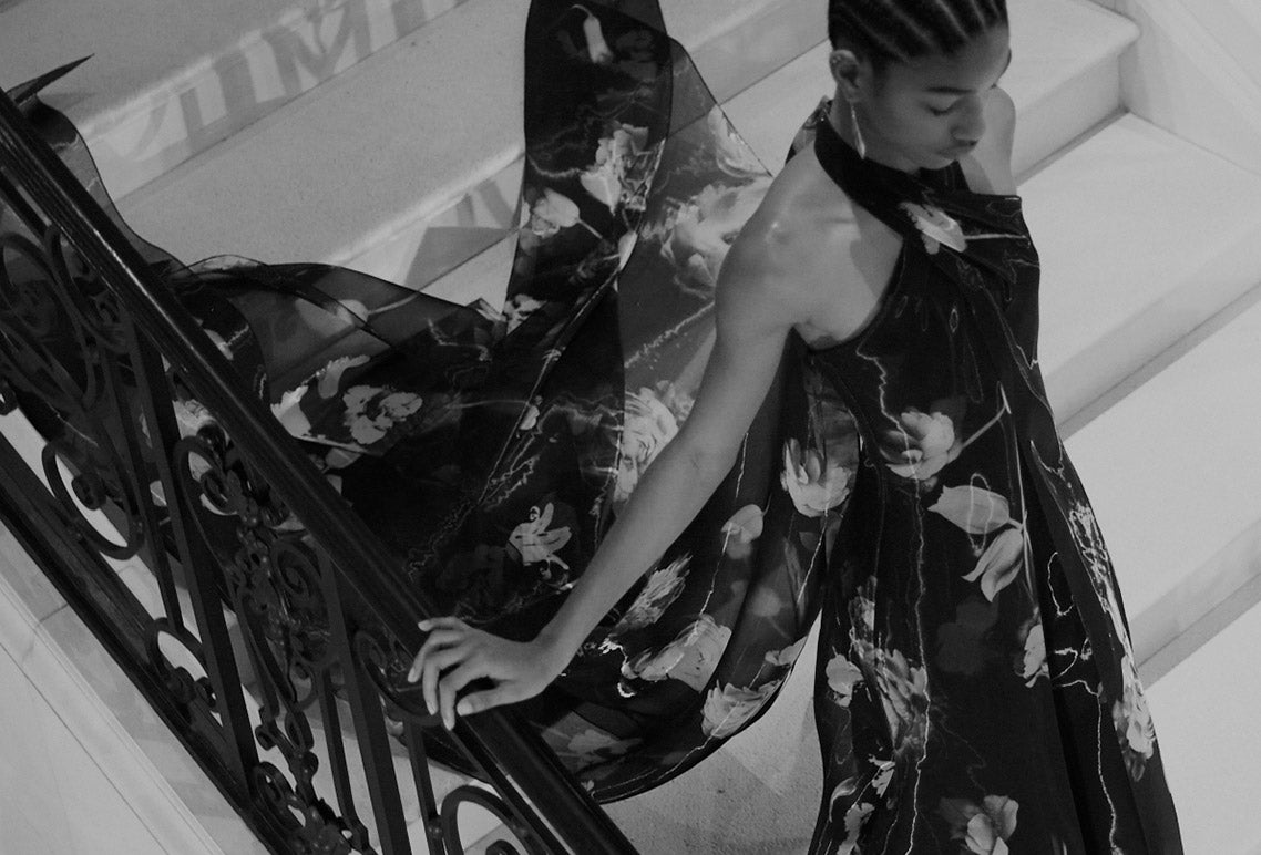 Model descending staircase in floral gown with train trailing behind her