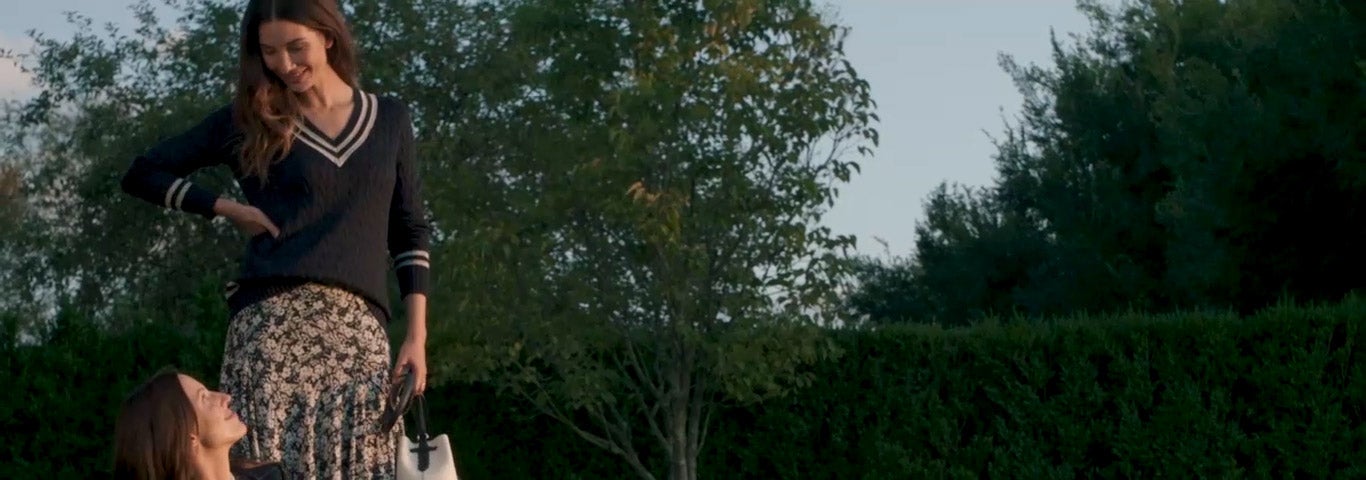 Woman wears plaid suit; woman wears cable-knit sweater and floral skirt.