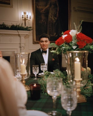 Man in tuxedo sitting at festively set dining table.