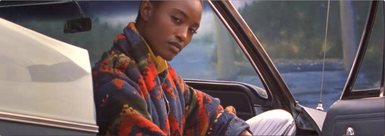 Woman in bright Southwestern-print shawl cardigan sits in car