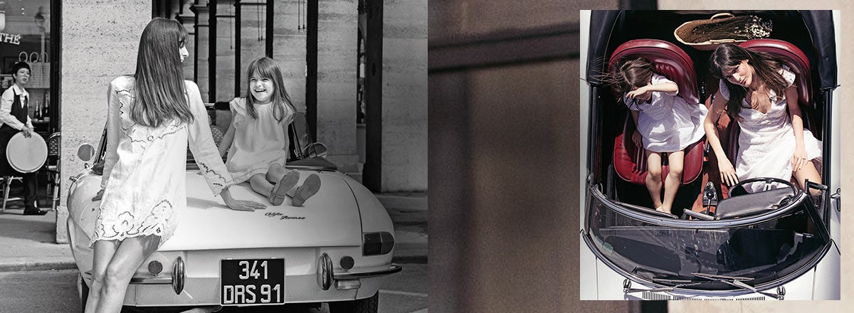 Mom and daughter in coordinating outfits sit on vintage car.