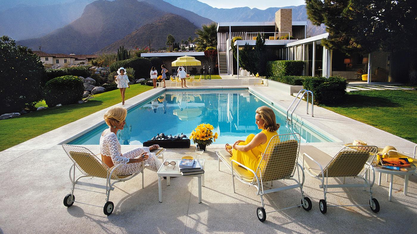  Casual conversation in an exquisite setting, elegantly illuminated by Slim Aarons’ artistic eye