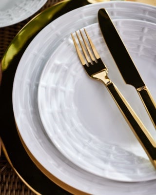 Golden-hued flatware on white porcelain plates with tonal pattern