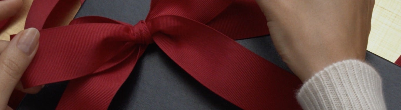 Woman placing Polo shirt in navy gift box with red ribbon