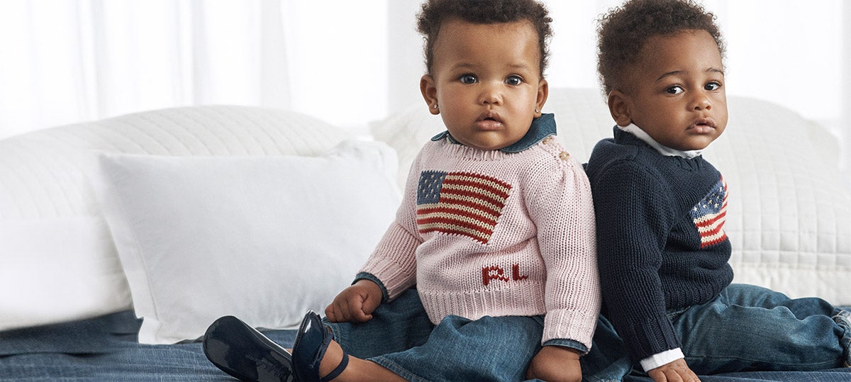 Baby boy and girl wear American flag sweaters and jeans.