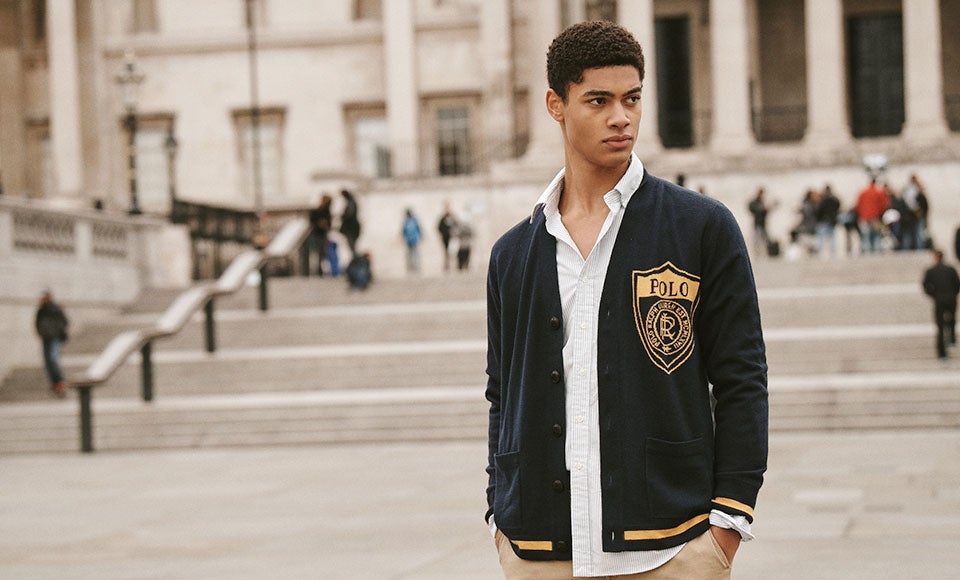 Man in navy cardigan with yellow stripes & crest graphic
