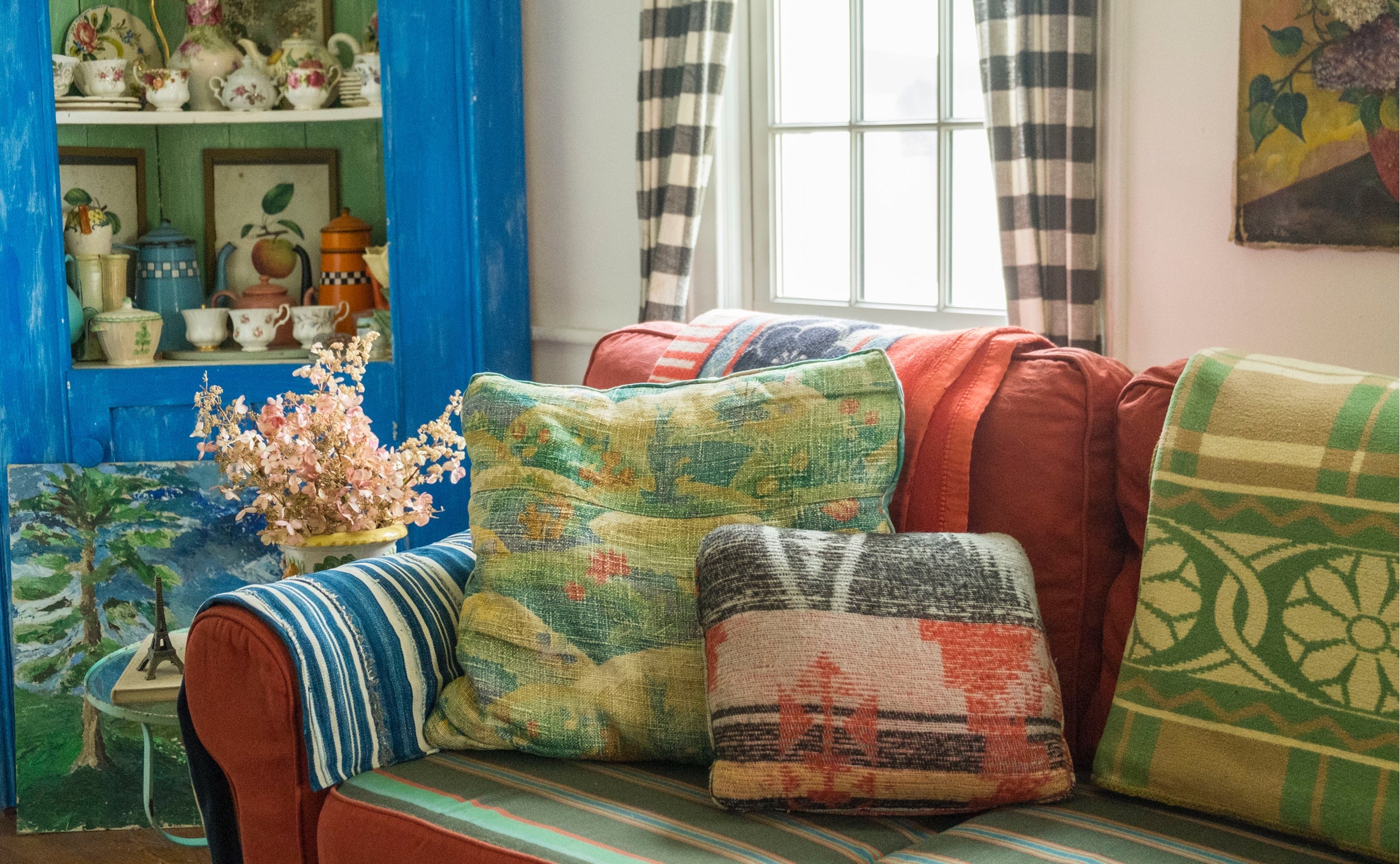 Instant character for a new sofa: layers of vintage blankets, textiles, and an eclectic pillow mix. The blue cupboard is filled with an a collection of English tea cups and vintage French coffee pots