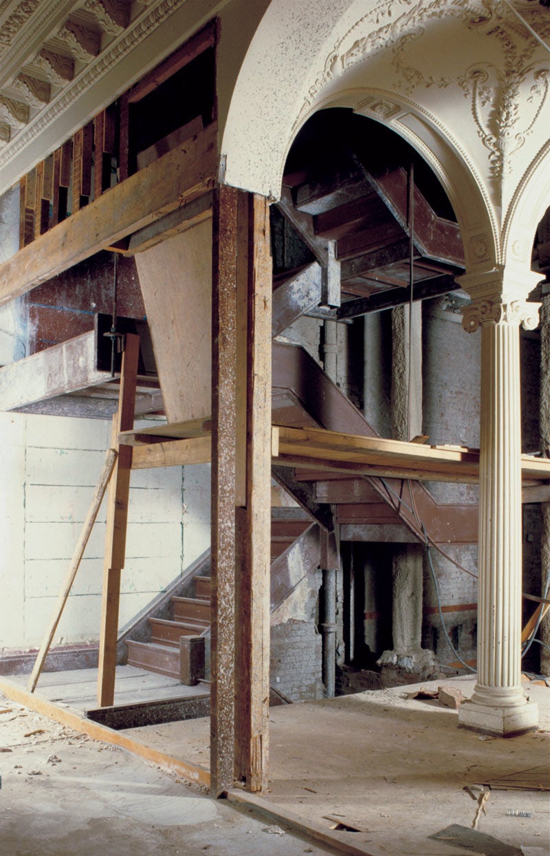 A vaulted ceiling, columns, and exposed staircase mid-renovation