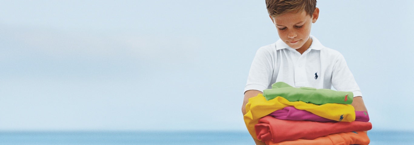Boy in white Polo shirt holds stack of colorful Polo shirts.
