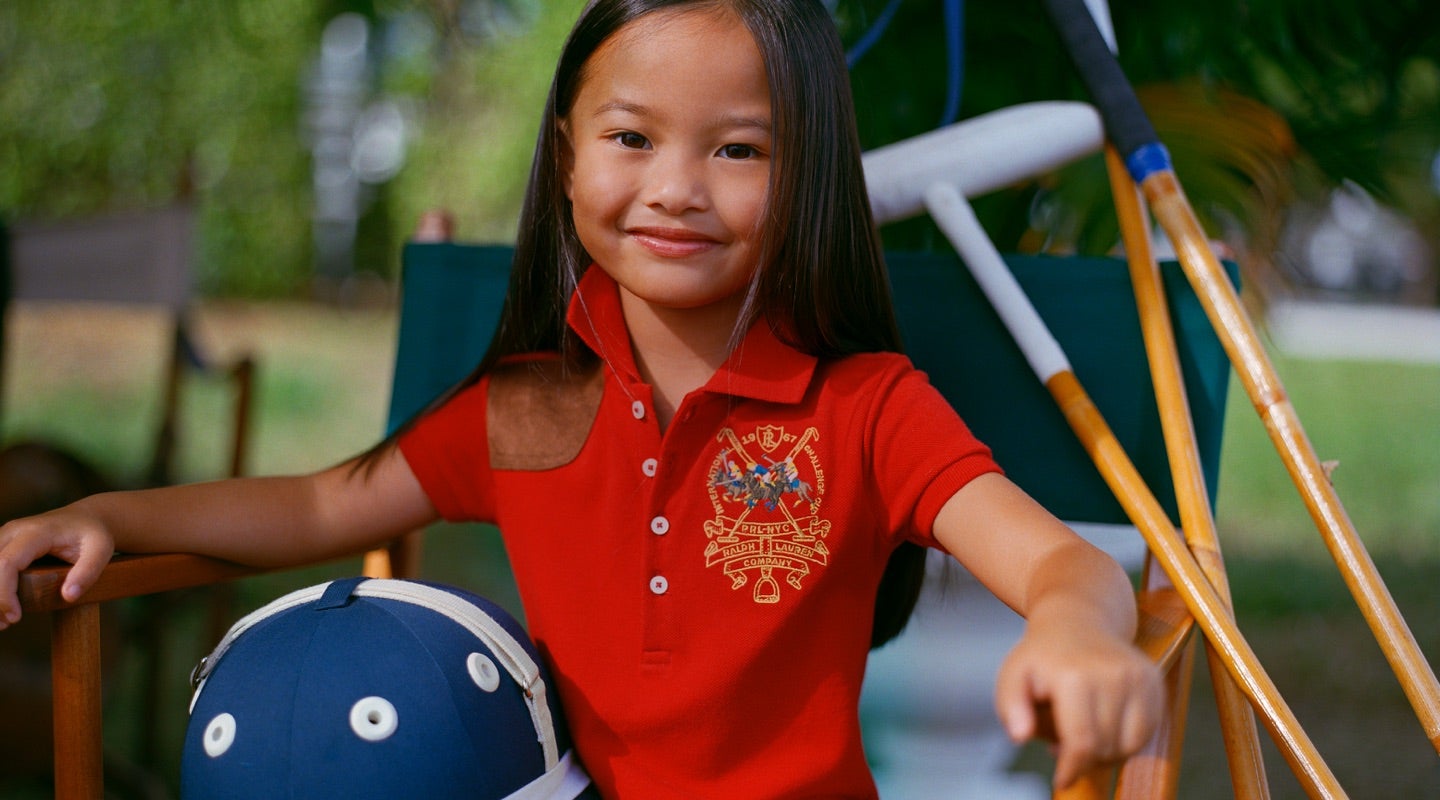 Girl wears red Polo shirt with equestrian-inspired graphic at chest.