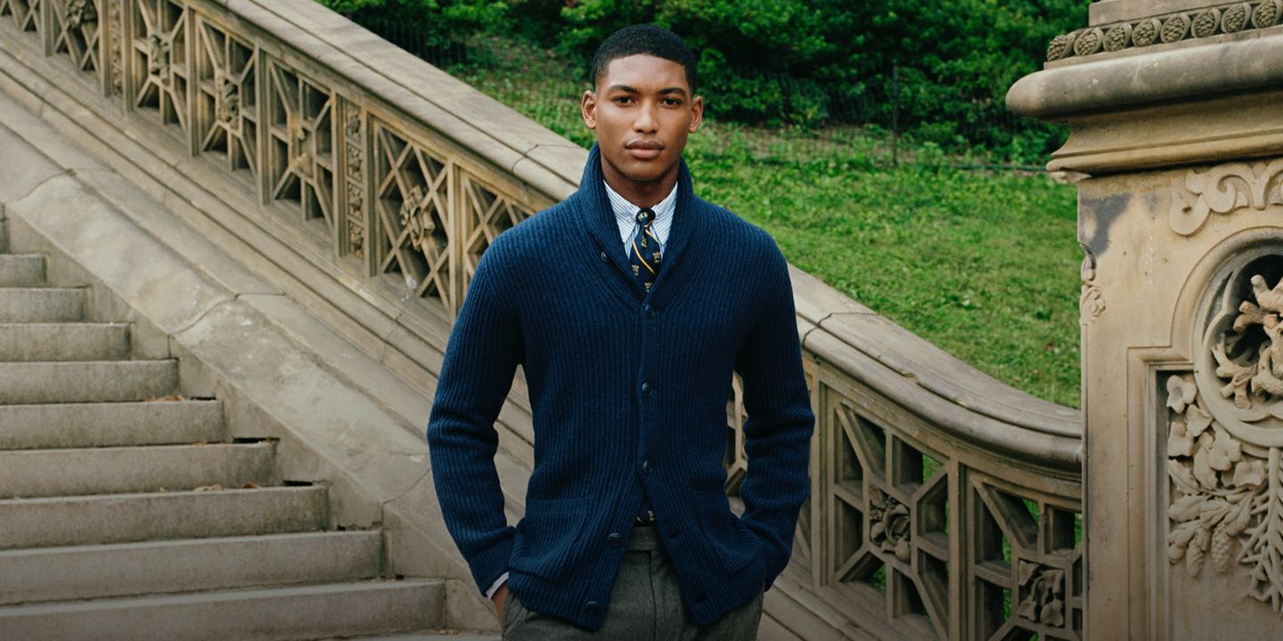 Man wears navy cardigan and tie on stone staircase.