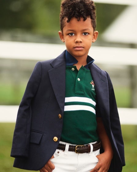 Boy with navy blazer over shoulders wears Polo shirt & white pants