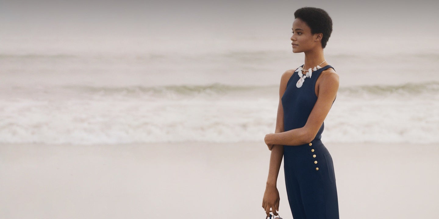 Woman in navy tank & trousers with gold buttoned side placket