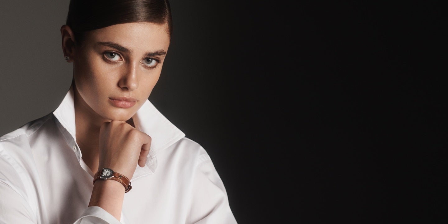 Woman wears watch with stirrup-shaped dial & brown leather strap