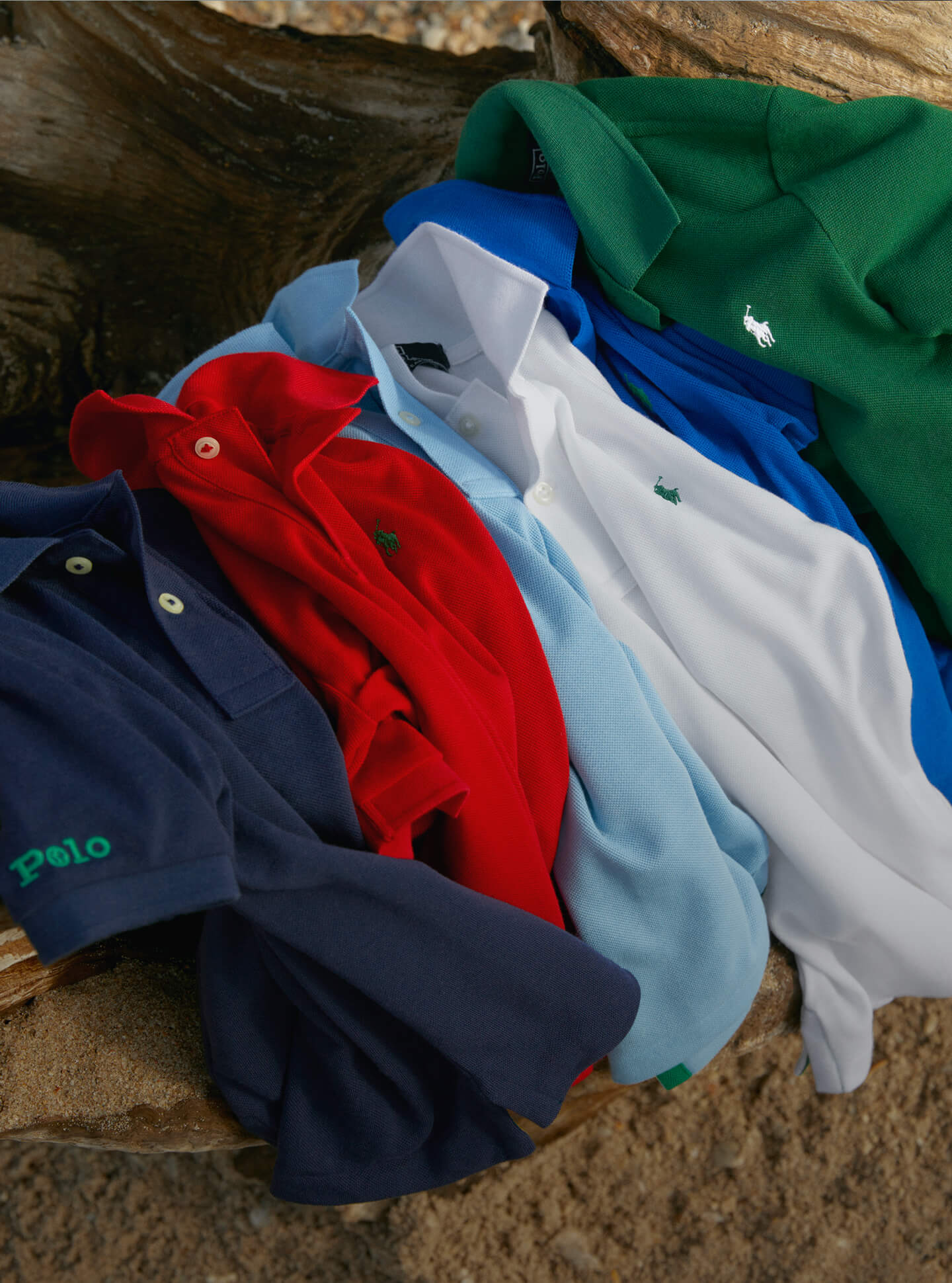 Earth Polo shirts in various colors on sandy beach.
