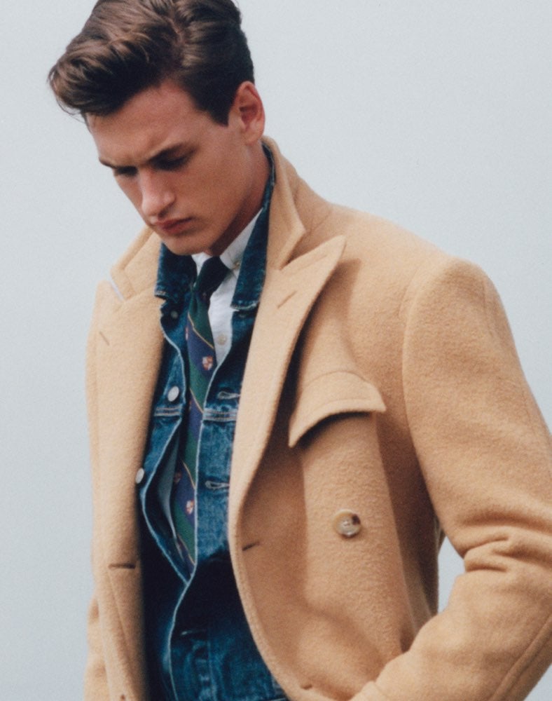 Man in tan peacoat layered over denim shirt
