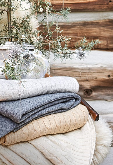 Stack of cable-knit throw blankets in muted winter hues